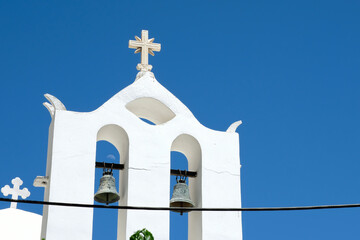 A cross with bells on the top of an orthodox whitewashed church in Ios Greece and a blue sky in the background in Ios Greece