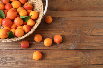 Wicker basket with fresh apricots on wooden background