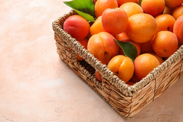Wicker box with fresh apricots on beige background