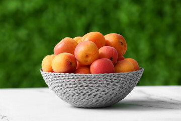 Wicker bowl with fresh apricots on white table outdoors