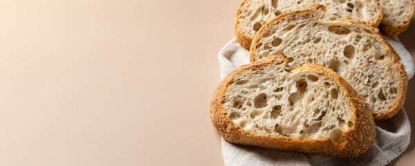 Close-up of slices of sourdough wheat bread on a linen towel on a beige background. Bakery products. Copy space wide banner.