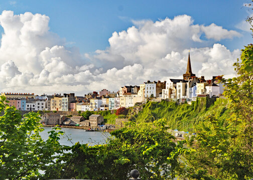 A beautiful panorama framed by green trees and bushes of the pretty resort town of Tenby in Wales with interesting white clouds