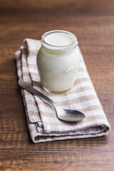 White yogurt in jar and spoon on checkered napkin.
