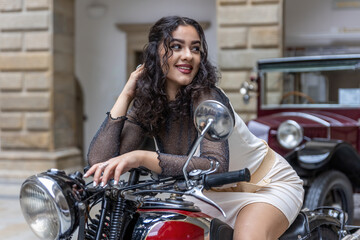 Fototapeta na wymiar Attractive young woman with long black hair is sitting in a sexy pose on vintage motorcycle. Horizontally. 