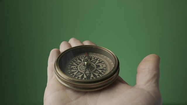 Compass on an open male palm on a green screen. The compass arrow points north. Direction and travel concept. HDR BT2020 HLG Material.