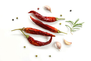 Red hot dry peppers, closeup on white background. Dried whole chili pods, peppercorns, fresh garlic cloves and rosemary herb. Aromatic and spicy organic ingredients.