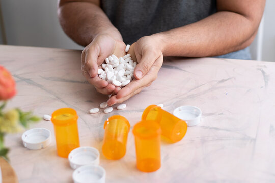Man holding with two hands a lot of medicine drugs over table with empty bottles