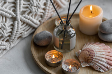 Obraz na płótnie Canvas Relaxation, detention zone in the living or bedroom. Stones, sea shells as decor. Apartment natural aroma diffusor with ocean breeze fragrance. Burning candles on bamboo tray, cozy home atmosphere.