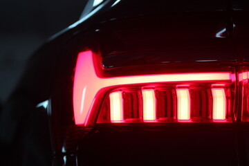 Car tail lights bright in the night/ Sports car rear profile background image, studio light. Car detail. LED taillights in hybrid sedan. With copy space. Neon lights in the night. Car in a dark city.