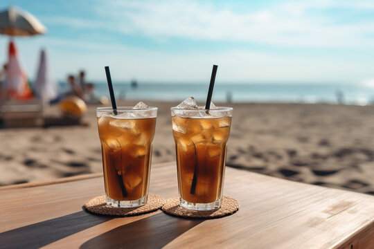 Two tall glasses of iced coffee or ice tea with ice and straws on the table on sandy tropical beach , summer vacation refreshment. High quality photo Generative AI