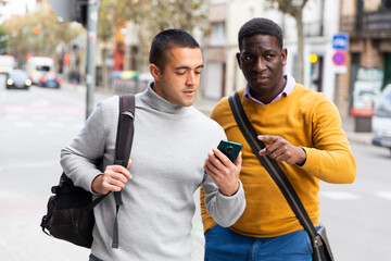 Caucasian man standing outdoors with smartphone and asking for directions African-american man.