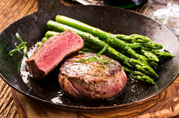Traditional roasted angus beef steak with with green asparagus served as close-up in a rustic frying pan - obrazy, fototapety, plakaty