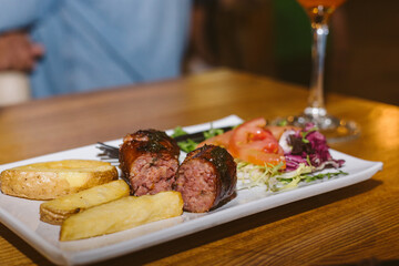small plate of grilled sausage ​​with salad and french fries on a bar table