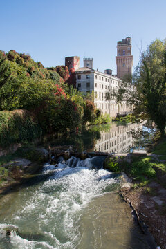 The Specola astronomical tower in Padua with historic architecture reflected in the canal on a clear sunny day, Padua, Italy