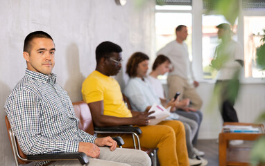 Adult man sitting on chair in lobby of legal aid agency or notary office, waiting for consultation...