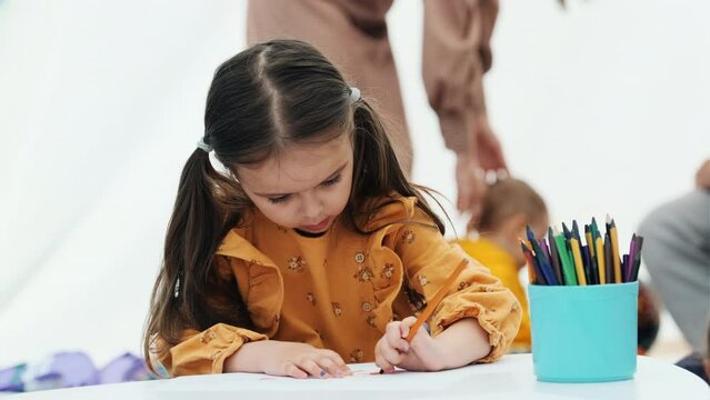 Kid girl painting with pencil. Kindergarten children education concept.