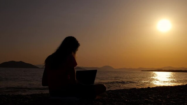 Girl silhouette finishing computer work. A girl silhouette stop her computer work to admire the nightfall beach in summer during vacation time.