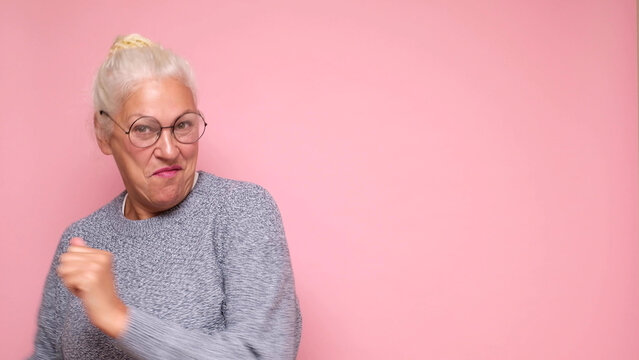 An elderly European woman in glasses confidently looks into the camera, smiling