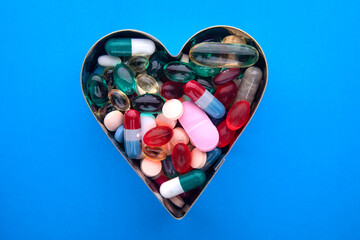 On the blue surface are pills and capsules in the shape of a heart. Healthy heart concept. - obrazy, fototapety, plakaty