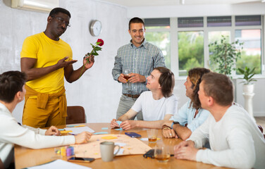 Happy African American man in love giving red rose to boyfriend during friendly get-togethers at home. Romantic atmosphere for same-sex couple, acceptance, and inclusivity concept