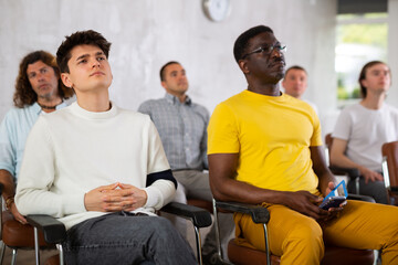 Interested motivated guy student listening with attention to lecture while studying with male coursemates in university auditorium