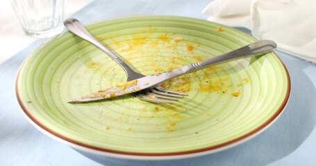 green dirty plate with fork and knife after eating. close-up. angle view. camera tracking. colored...