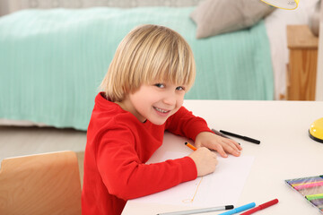 Little boy drawing at desk in room. Home workplace