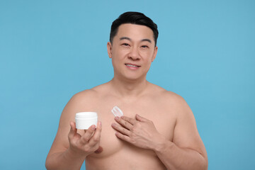 Handsome man applying body cream onto his chest on light blue background