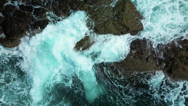 Vitality of green energy sea and clear ocean water. Top view colorful waters of the ocean, swirl around the rocky and scenic coastline. Sea waves breaking over rocks mountains. 4K