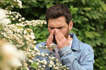 Man suffering from seasonal pollen allergy near blossoming tree on spring day