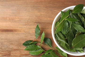 Aromatic fresh bay leaves and bowl on wooden table, flat lay. Space for text