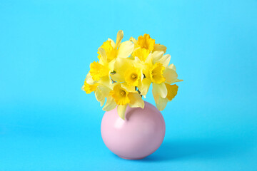 Bouquet of beautiful yellow daffodils in vase on light blue background