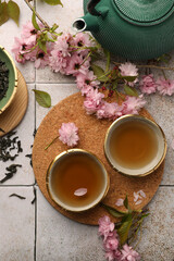 Traditional ceremony. Cup of brewed tea, teapot, dried leaves and sakura flowers on tiled table, flat lay