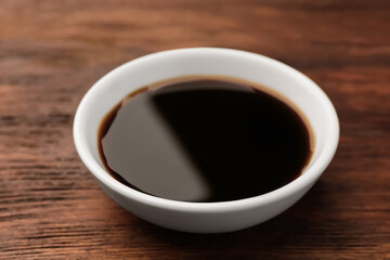 Bowl with soy sauce on wooden table, closeup