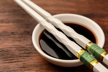 Bowl with soy sauce and chopsticks on wooden table, closeup