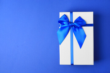 Beautiful gift box with bow on blue background, top view. Space for text