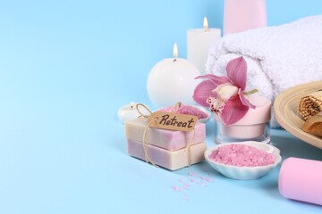 Retreat concept. Burning candles, orchid flower and different spa products on light blue background. Space for text