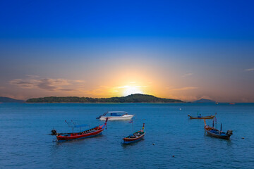 Sunset over Rawai Beach in Phuket island Thailand. Lovely turquoise blue waters, lush green mountains colourful skies and beautiful views the pier and long tail boats. Sky is taken seperate from Body 