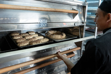 A young Hispanic baker is opening the door open to check the sweet breads baking time