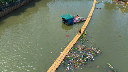 A polluted river with a garbage trap and workers cleaning up the river. Jakarta, Indonesia.
