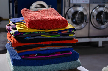 Stack of colorful cotton clothes in an industrial laundry with washing machines behind.
