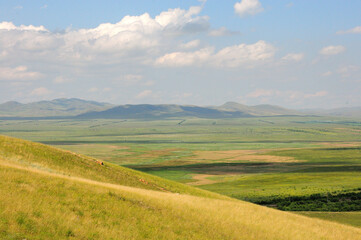 Obraz premium View of the picturesque endless steppe from the top of a high hill and a mountain range on the horizon on a sunny summer day.