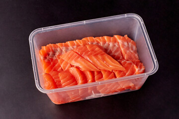 Sliced fresh salmon prepared and arranged in a clear plastic food box isolated on black background, packaging food for take away.