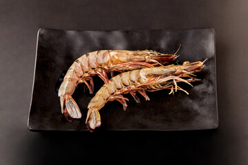 2 fresh tiger prawns placed on a black plate isolated on black background.