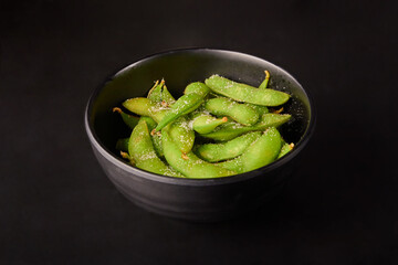 Green Japanese Soybeans (Edamame) top with salt on black bowl isolated on black background.
