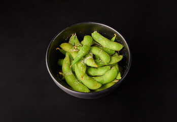 Green Japanese Soybeans (Edamame) top with salt on black bowl isolated on black background.
