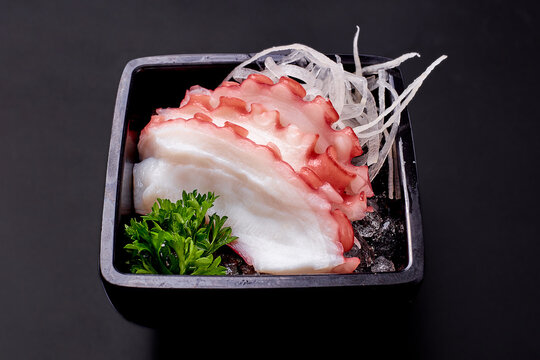 Sliced tako sashimi and radish on ice in a black plate isolated on black background. Sliced boiled squid, popular Japanese food