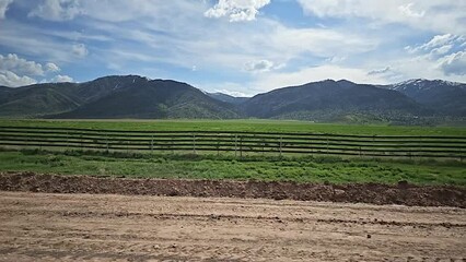 Drive Plate-Side-Slowly passing road construction, Green fields and Distant Mountains under a cloudy sky.