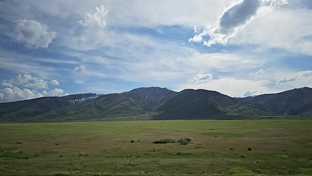 Drive Plate-Side-Slowly passing green fields with distant mountains under scattered cloudy sky