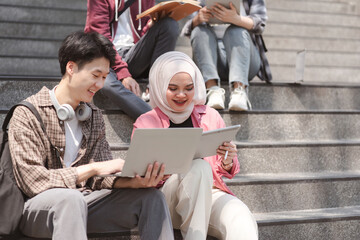 A multiethnic group of university students is studying together while sitting on steps near the campus and communicating with each other.